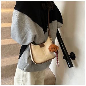 Detail of creamy white faux leather hobo bag with brown trim and cute plush puppy charm
