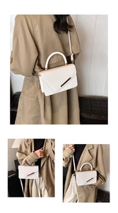 Close-up of white lychee leather handbag with gold metal bar worn with beige trench coat
