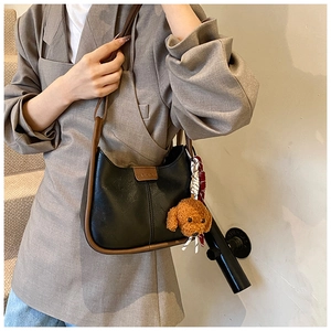 Detail of black faux leather shoulder bag with FASHION label and teddy bear charm accessory