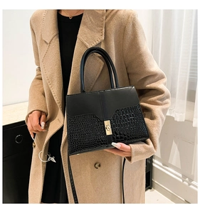 Detail of black crocodile pattern handbag on beige coat with golden metal clasp