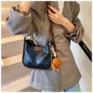 Detail of matte black leather handbag featuring contrast trim and a plush bear charm