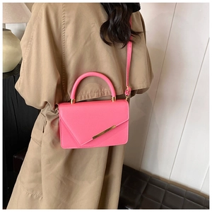 Pink lychee grain leather handbag with gold metal bar detailing and handle worn with coat