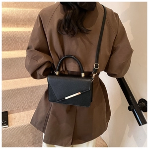 Detail of black pebbled leather crossbody bag with asymmetric flap and gold metal bar