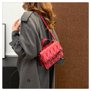 Détail d'un sac à main rouge matelassé avec chaîne en résine sur trench gris