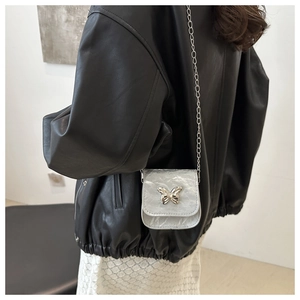 Detail of silver mini chain bag featuring metallic butterfly buckle and pleated texture
