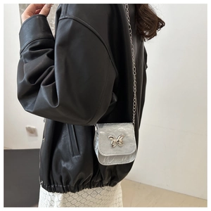 Detail view of mini silver crossbody bag with a butterfly clasp on a black leather jacket