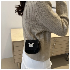 Detail of a mini black crossbody bag featuring a silver butterfly buckle and chain strap