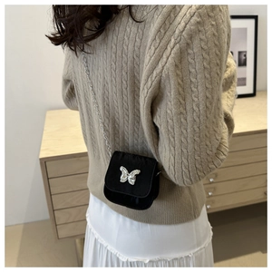 Detailed view of mini black crossbody bag featuring a silver butterfly buckle and chain strap