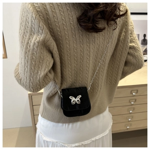 Detailed view of a mini black crossbody bag with silver butterfly buckle and chain strap