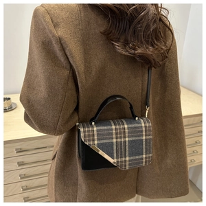 Detail of a vintage plaid crossbody bag with gold metal trim worn over a brown coat