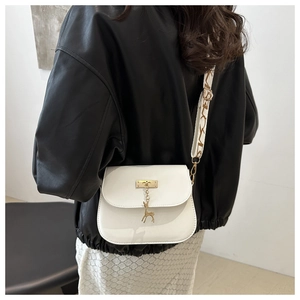 Detail view of a white crossbody bag featuring a golden deer charm and patterned strap