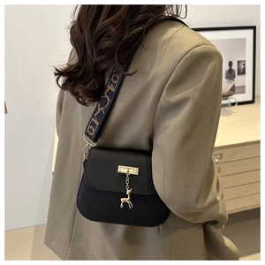 Detail of black crossbody bag with golden deer pendant and decorative wide textile strap