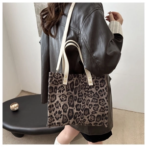 Close-up of leopard print tote bag with white leather straps worn by model in brown leather coat