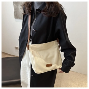 Détail du sac bandoulière minimaliste en toile beige avec sangle et logo en cuir marron