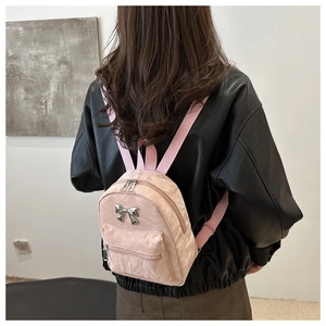 Pink mini backpack with silver bow detail and pleated fabric shown on a model's back