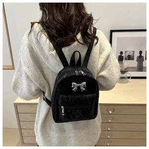 Close-up of a black mini backpack with a shiny silver metal bow and textured fabric finish