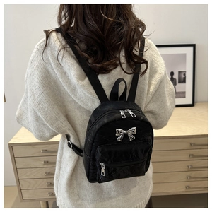 Detail showing a black mini bow backpack with glossy crinkled texture on a casual model
