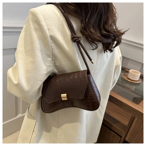 Detail of dark brown faux leather shoulder bag with crocodile pattern and golden metal buckle