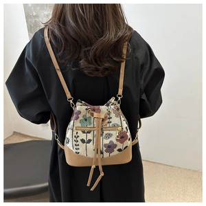 Detailed view of floral jacquard canvas bucket bag with camel leather straps on person