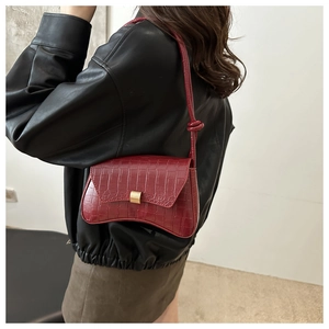 Detail view of burgundy croc-embossed shoulder bag featuring a unique curved base and gold clasp