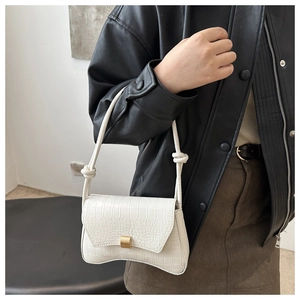 Detail of white crocodile-textured underarm bag with gold buckle and knot accents