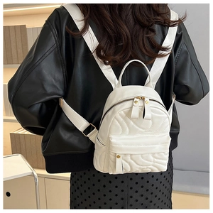 Detail of white quilted mini backpack with gold zippers shown on model's back