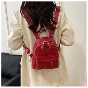 Close-up of a red mini quilted backpack with gold zippers shown on a model's back