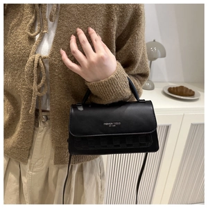 Detail of black crossbody bag featuring silver text and woven texture in a lifestyle setting