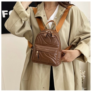 Detail of a brown quilted mini backpack with gold zippers worn over a beige trench coat