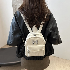 Chic cream white mini backpack with metal bow detail shown on model from back view