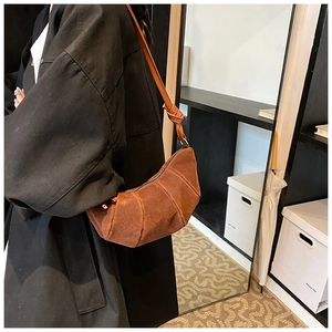 Dettaglio di una borsa a mezzaluna in camoscio marrone con trama a pieghe e tracolla annodata