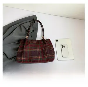 Detail of red and green plaid woolen shoulder bag with brown leather handles and gold metal clips