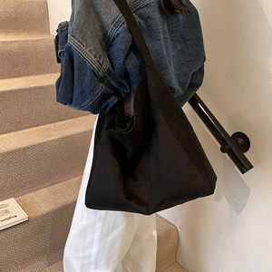 Large black minimalist tote bag with wide strap shown on model in a modern staircase