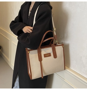 Detail of canvas tote bag with brown leather trim and shoulder strap on black coat