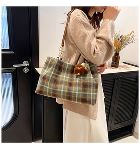 Detail of plaid tote bag with brown leather strap and fuzzy charm on shoulder