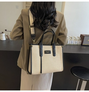 Detailed back view of a beige canvas tote with black leather trim and woven strap