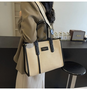 Detail view of large canvas tote bag with black leather trim and wide shoulder strap