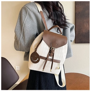 Détail du sac seau matelassé beige avec rabat en cuir marron et pendentif smiley