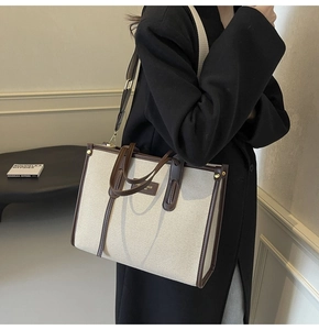 Detail of a large canvas tote with brown leather trim styled on a black wool coat