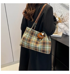 Detail of plaid tote bag with brown leather strap and plush monster charm decoration