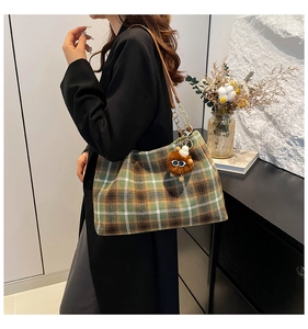 Detail of plaid tote bag featuring brown leather shoulder strap and plush charm