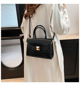 Detail of black crossbody bag featuring gold buckle and crocodile texture side panels