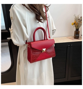 Detail of red envelope bag featuring crocodile texture and golden triangular metal clasp