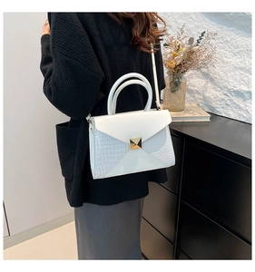 Detail view of white croc-embossed leather handbag with gold rivet and envelope flap design