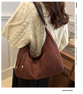 Gros plan du sac hobo en daim marron avec pompon sur un mannequin en pull blanc