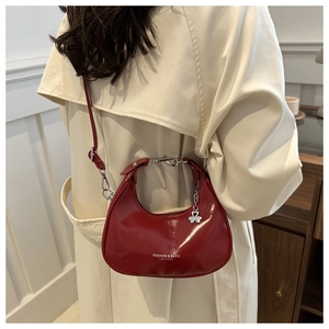 Close-up of red patent leather crescent bag with silver clover charm and logo detail