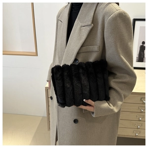 Nahaufnahme der schwarzen Kunstfell-Plissee-Clutch kombiniert mit einem beigen Wollmantel
