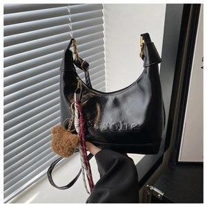 Detail of black glossy hobo bag with isohue embossing and a cute bear plush charm