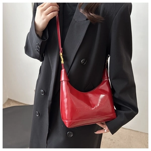Detail of glossy red patent leather underarm bag with embossed letters and gold hardware
