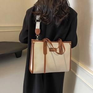 Large beige canvas tote bag with brown leather trim and wide crossbody strap on model